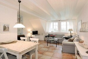 A cozy living room with a dining table, striped sofa, and a television. - Sonnenkuhle - Ameland 09 (Wenningstedt - Braderup)