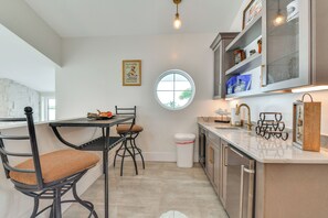 A modern kitchen with a dining area, featuring a round window, a trash bin, and a framed picture on the wall. - Luxury Bayfront Home, Private Dock, Steps to Beach (Englewood)
