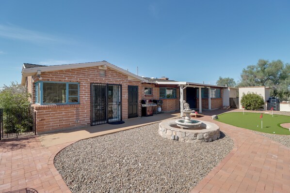 A brick house with a patio, a barbecue area, and a small garden with a fountain. - Pool, Putting Green & Mtn Views: Tucson Home (Tucson)