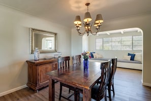 A dining area with a wooden table, chairs, a chandelier, a mirror, and a window with a view. - Pool, Putting Green & Mtn Views: Tucson Home (Tucson)