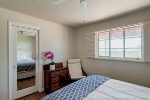 A bedroom with a bed, a chair, a dresser, a window with shutters, and a door leading to another room. - Pool, Putting Green & Mtn Views: Tucson Home (Tucson)
