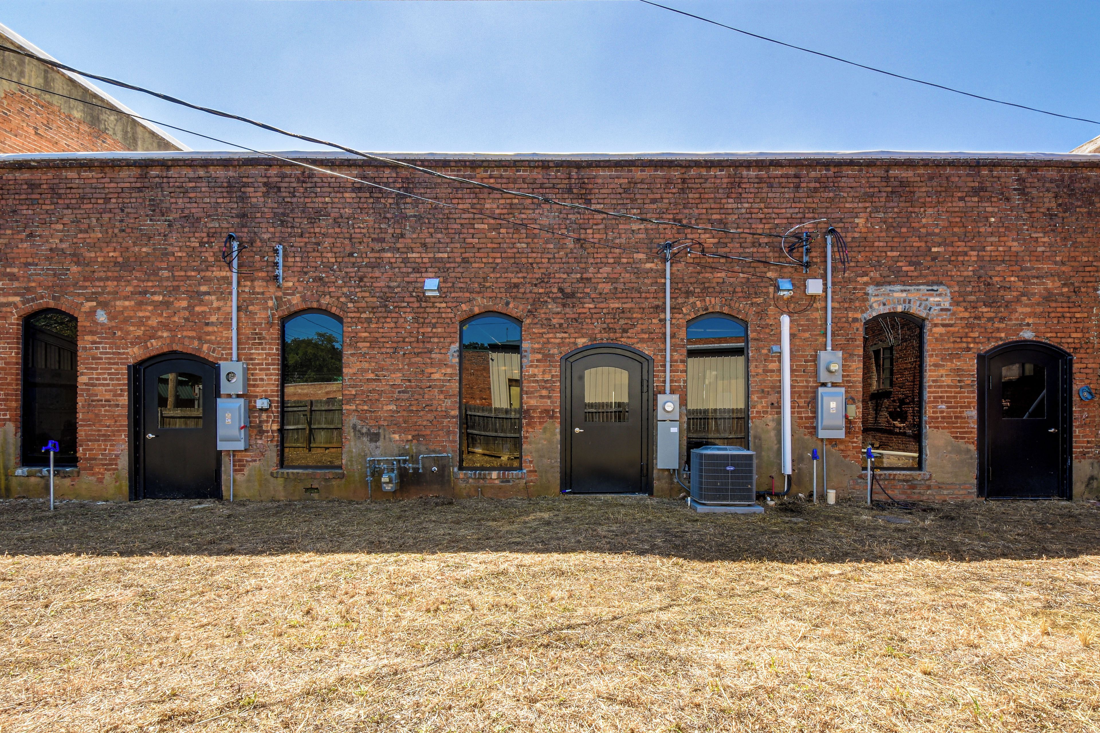 A brick building with multiple arched doorways and windows, utility meters, and outdoor electrical equipment.