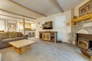 A living room with a sofa, coffee table, fireplace, television, and kitchen area in the background. - Steps to Slopes! Mammoth Mountain Condo (Mammoth Lakes)
