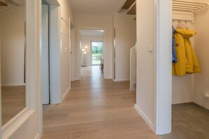 A corridor with a wooden floor, white walls, and a door leading to a room with a window. - Holiday apartment with 1 bedroom (Aurich)