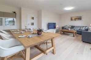 A modern living room with a wooden dining table set for tea, a grey sofa, and a flat-screen TV. - Holiday apartment with 1 bedroom (Aurich)