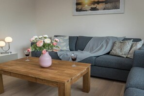 A living room with a wooden coffee table, a grey sofa, and a pink vase with flowers. - Holiday apartment with 1 bedroom (Aurich)
