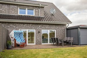 A house with a brick exterior, a tiled roof, a sliding glass door, and a patio with outdoor furniture. - Holiday apartment with 1 bedroom (Aurich)