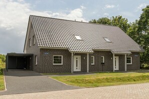 Een gebouw met twee verdiepingen, een pannendak, een overdekte garage en een verharde oprit.