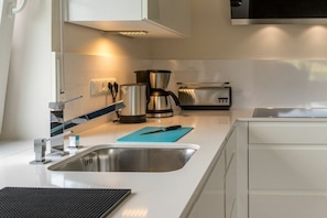 A modern kitchen with a stainless steel sink, a coffee maker, a toaster, and a knife on a blue cutting board. - Holiday apartment with 1 bedroom (Aurich)