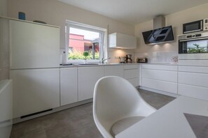 A modern kitchen with white cabinetry, a built-in oven, microwave, and a TV mounted above the counter. - Holiday apartment with 1 bedroom (Aurich)