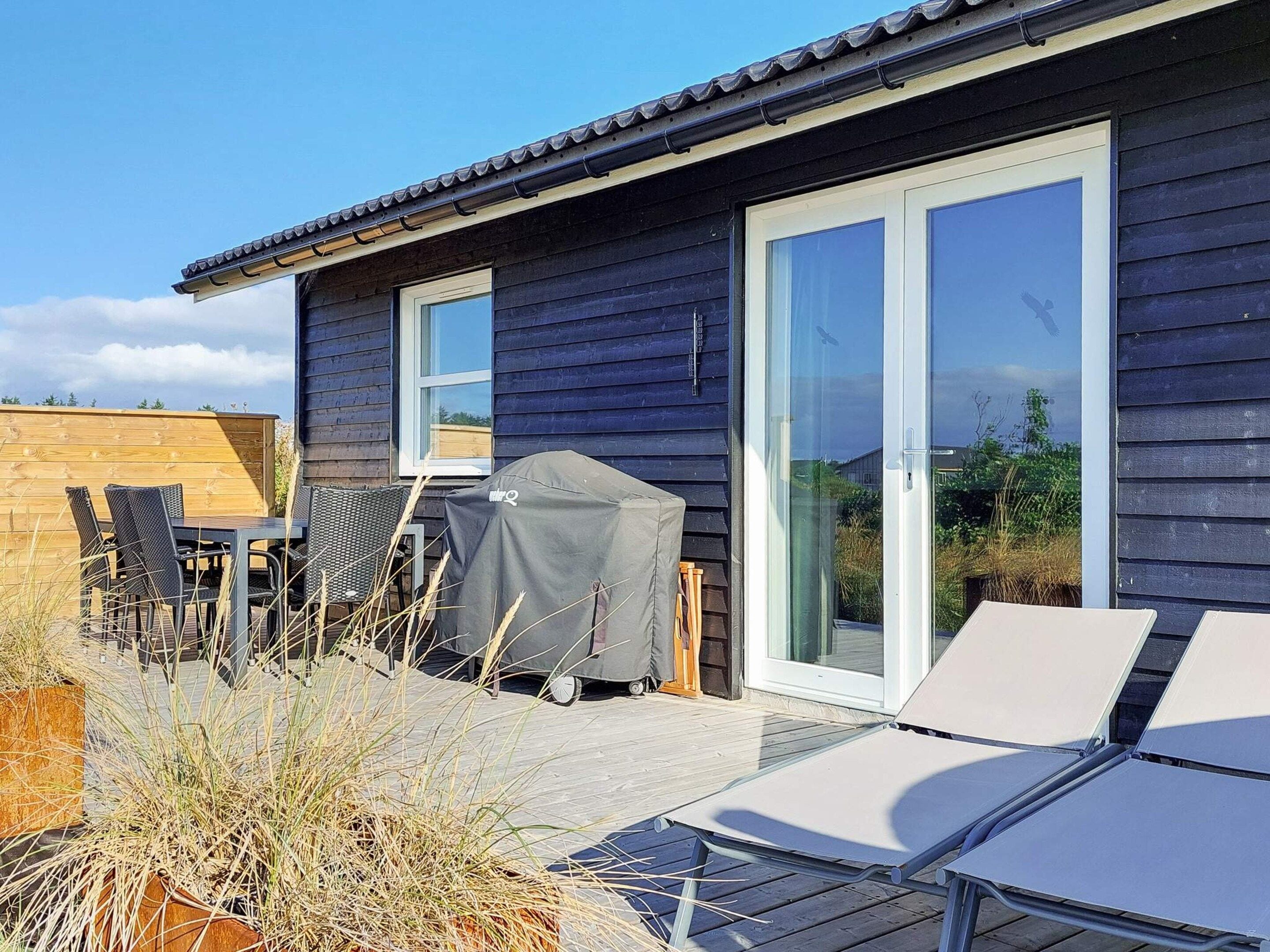 A house with a patio area, including a table with chairs, a barbecue grill, and a covered grill.