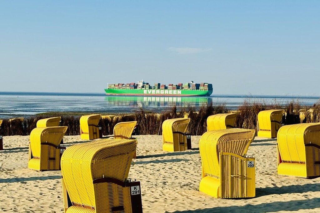 A beach with yellow wicker chairs and a green cargo ship in the background.