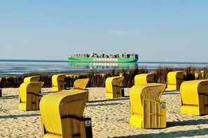 A beach with yellow wicker chairs and a green cargo ship in the background. - Holiday apartment with 1 bedroom (Cuxhaven)