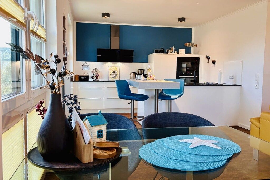A modern kitchen with a blue accent wall, a dining area with blue chairs, and a glass table with starfish placemats.
