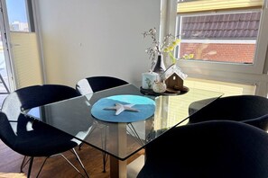 A modern dining area with a glass table, black chairs, a starfish placemat, and a vase with flowers. - Holiday apartment with 1 bedroom (Cuxhaven)