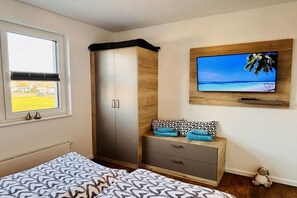 Een slaapkamer met een bed, een kledingkast, een aan de muur bevestigde televisie en een raam met uitzicht.