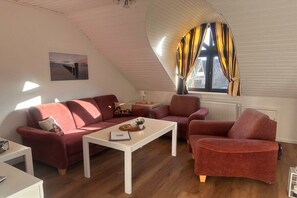 Ein Wohnzimmer mit einem roten Sofa, einem weißen Couchtisch und einem Fenster mit Vorhängen.