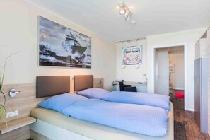 Una cama doble con cabecera, una mesita de noche, un televisor montado en la pared y un cuadro enmarcado sobre la cama.
