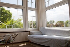 A room with a large window, a sofa, and a table with a teapot. - Holiday home with 4 bedrooms (Jemgum-Ditzum)
