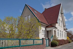 A two-story house with a red-tiled roof, a brick facade, and a green fence. - Holiday home with 4 bedrooms (Jemgum-Ditzum)