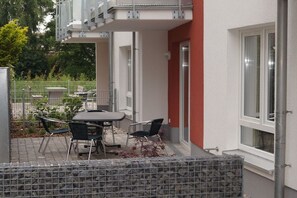 An outdoor patio with a table and chairs, a stone wall, and a red building facade. - HUS PIA Apt. 2 "Neuwerk" (Cuxhaven)