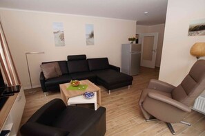 A modern living room with a black sectional sofa, a brown armchair, and a small table with a bowl of fruit. - HUS PIA Apt. 2 "Neuwerk" (Cuxhaven)