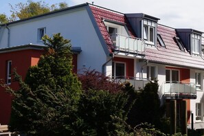 Ein zweistöckiges Wohngebäude mit rotem Dach, weißen Wänden und einem Balkon im oberen Stockwerk.