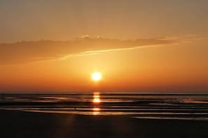 Um pôr do sol sobre uma praia, com águas calmas refletindo o sol.