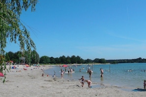 A beach with people swimming and walking on the sand, tents, and umbrellas set up. - Lüttje Huck/ Seeblick 2 (Aurich)