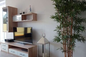 Ein modernes Wohnzimmer mit einem Flachbildfernseher, Holzregalen, einer dekorativen Laterne und einer hohen Bambuspflanze.