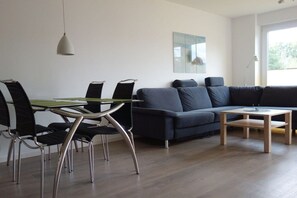 Ein modernes Wohnzimmer mit einem dunkelblauen Sofa, einem Glastisch mit Stühlen und einem kleinen Holztisch.