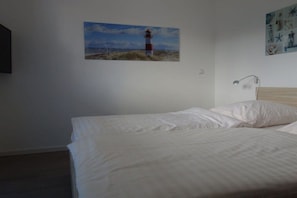 Ein Schlafzimmer mit einem Bett, einem an der Wand befestigten Bild von einem Leuchtturm und einer kleinen Nachttischlampe.