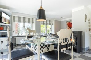 Ein Essbereich mit einem Glastisch, Stühlen mit Karomuster, einer schwarzen Pendelleuchte und einem Kamin.