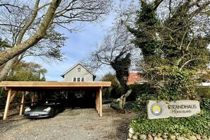 Ein Anwesen mit überdachtem Parkplatz, einem Schild mit der Aufschrift 'STRANDHAUS LONG ISLAND' und einem Gebäude mit Satteldach.