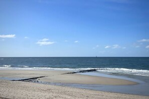 Ein Strand mit blauem Himmel, ruhiger See und einem fernen Leuchtturm.
