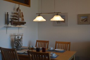 A dining area with a wooden table, chairs, and hanging pendant lights. - Freeport on the South Beach (Fehmarn)