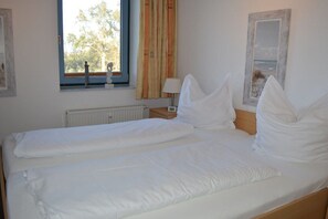 A double bed with white bedding in a room with a window, a radiator, and a lamp on a bedside table. - Freeport on the South Beach (Fehmarn)