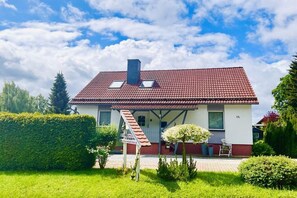 Ein eingeschossiges Haus mit rotem Ziegeldach, Schornstein und einer kleinen Veranda mit einem Stuhl.