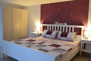 Een slaapkamer met een bed, nachtkastjes, een garderobe en een hoofdeinde met bloemenmotief.