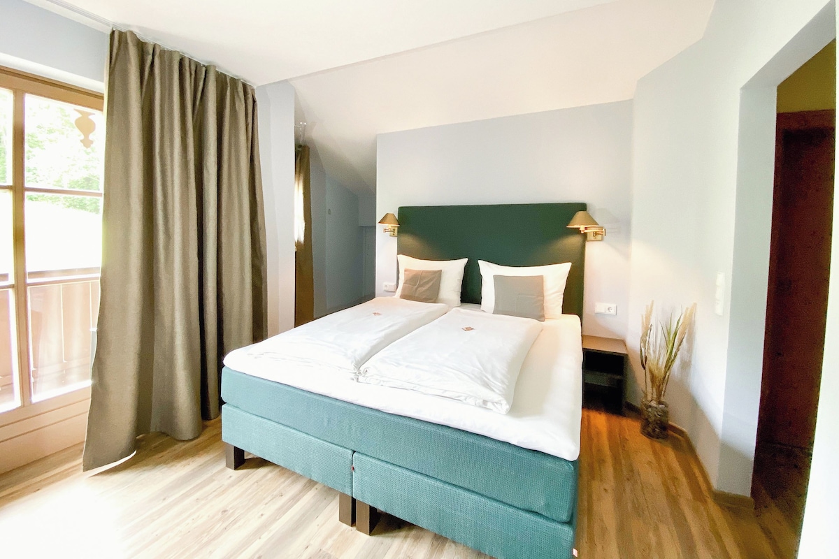 Ein Hotelzimmer mit einem Bett, einem Nachttisch, einer Lampe und Blick ins Freie.