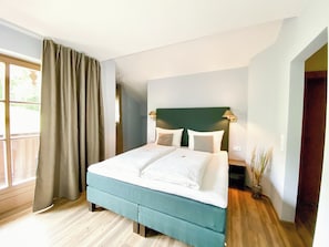 Ein Hotelzimmer mit einem Bett, einem Nachttisch, einer Lampe und Blick ins Freie.