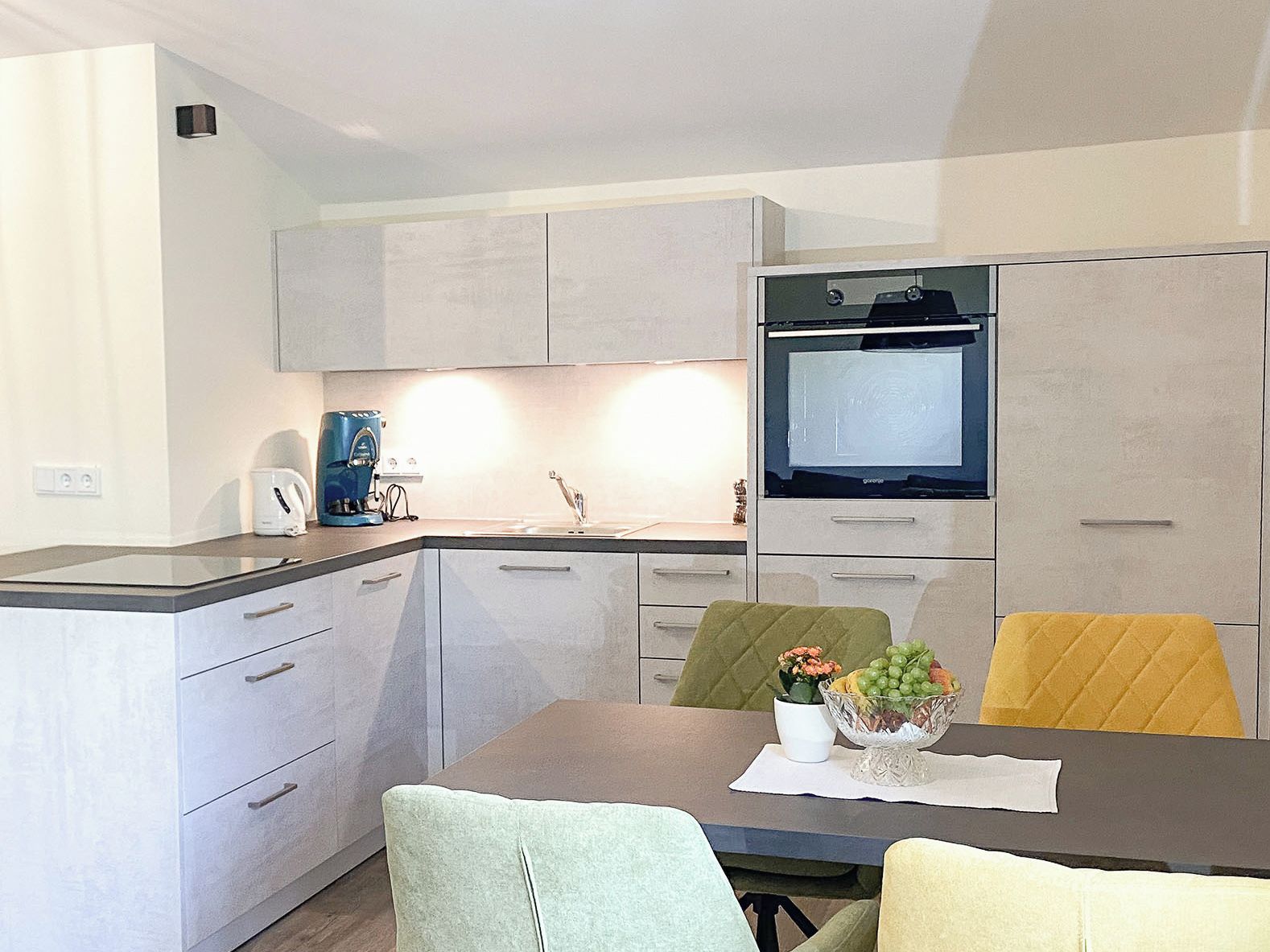Una cocina moderna con horno integrado, cafetera y comedor con mesa y sillas.