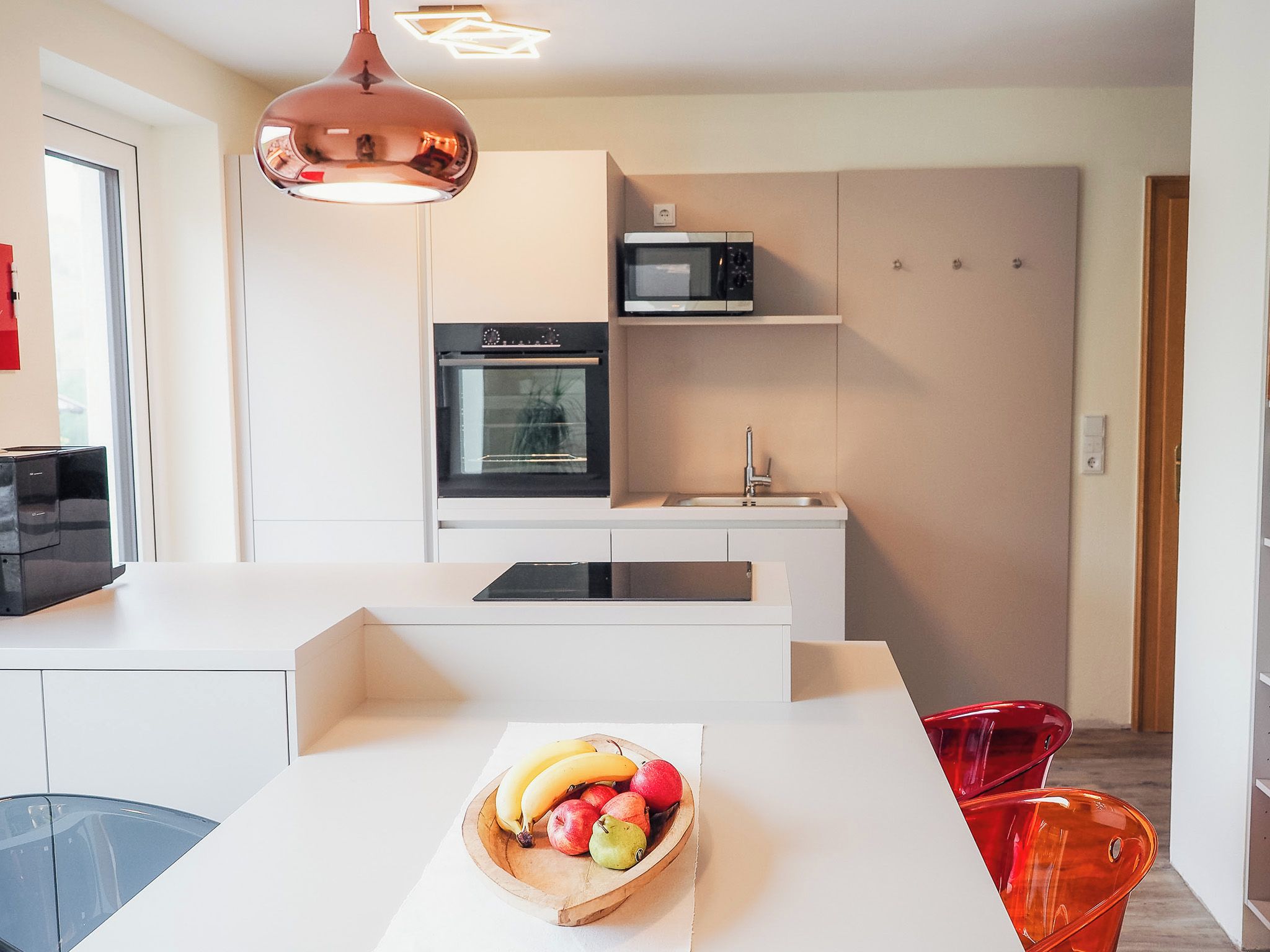 A modern kitchen with white cabinetry, a built-in oven, a microwave, and a fruit bowl on the counter.