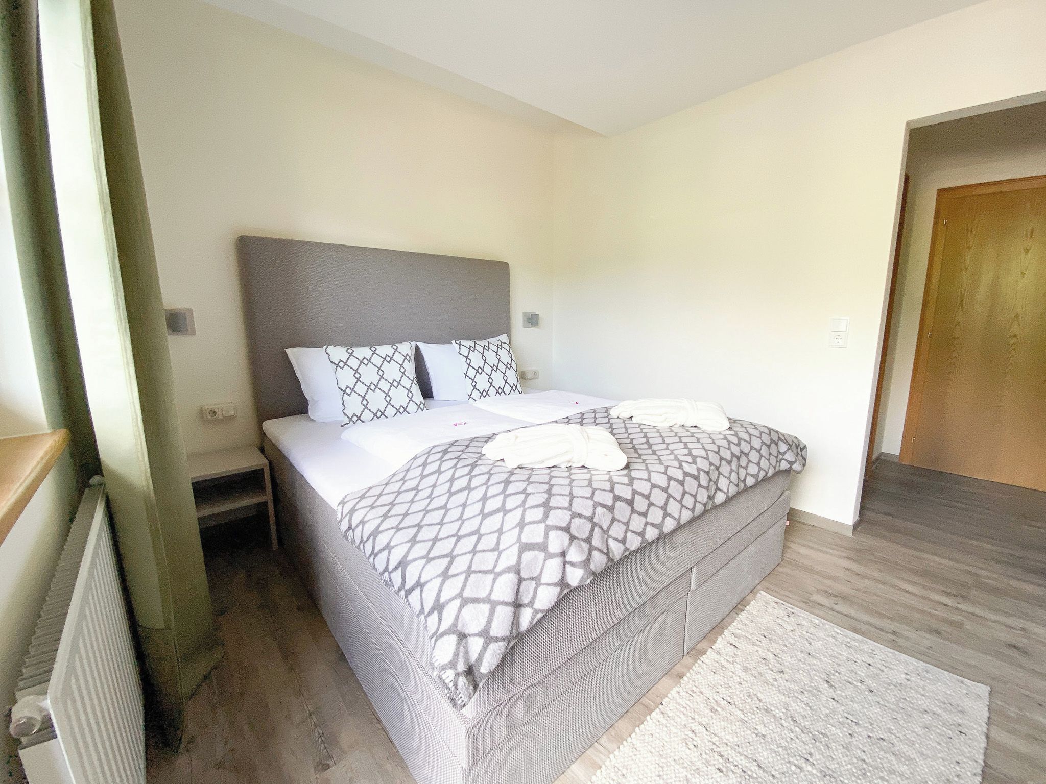 A single-bed room with a grey headboard, a patterned bedspread, and a white throw blanket.