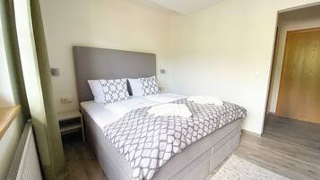 A single-bed room with a grey headboard, a patterned bedspread, and a white throw blanket.
