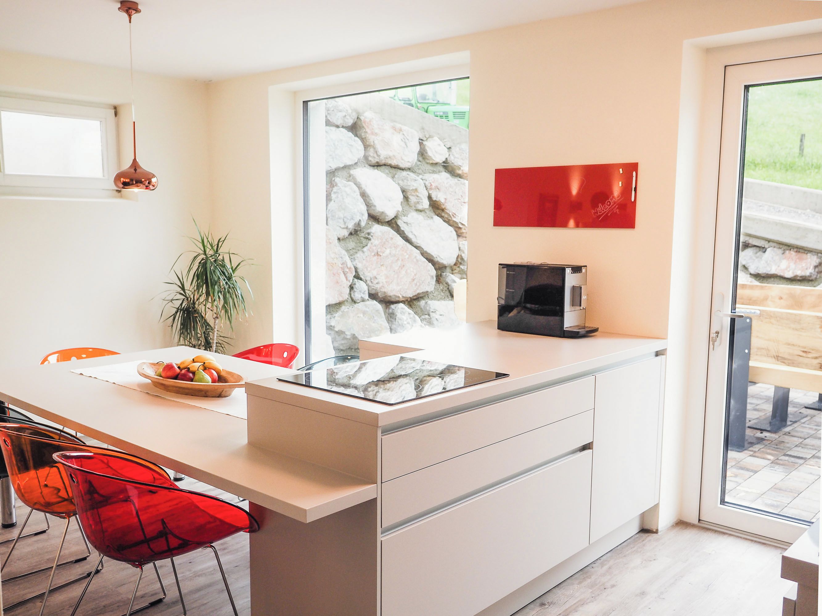 A modern kitchen with a large island, a stone wall, and a red wall decoration.