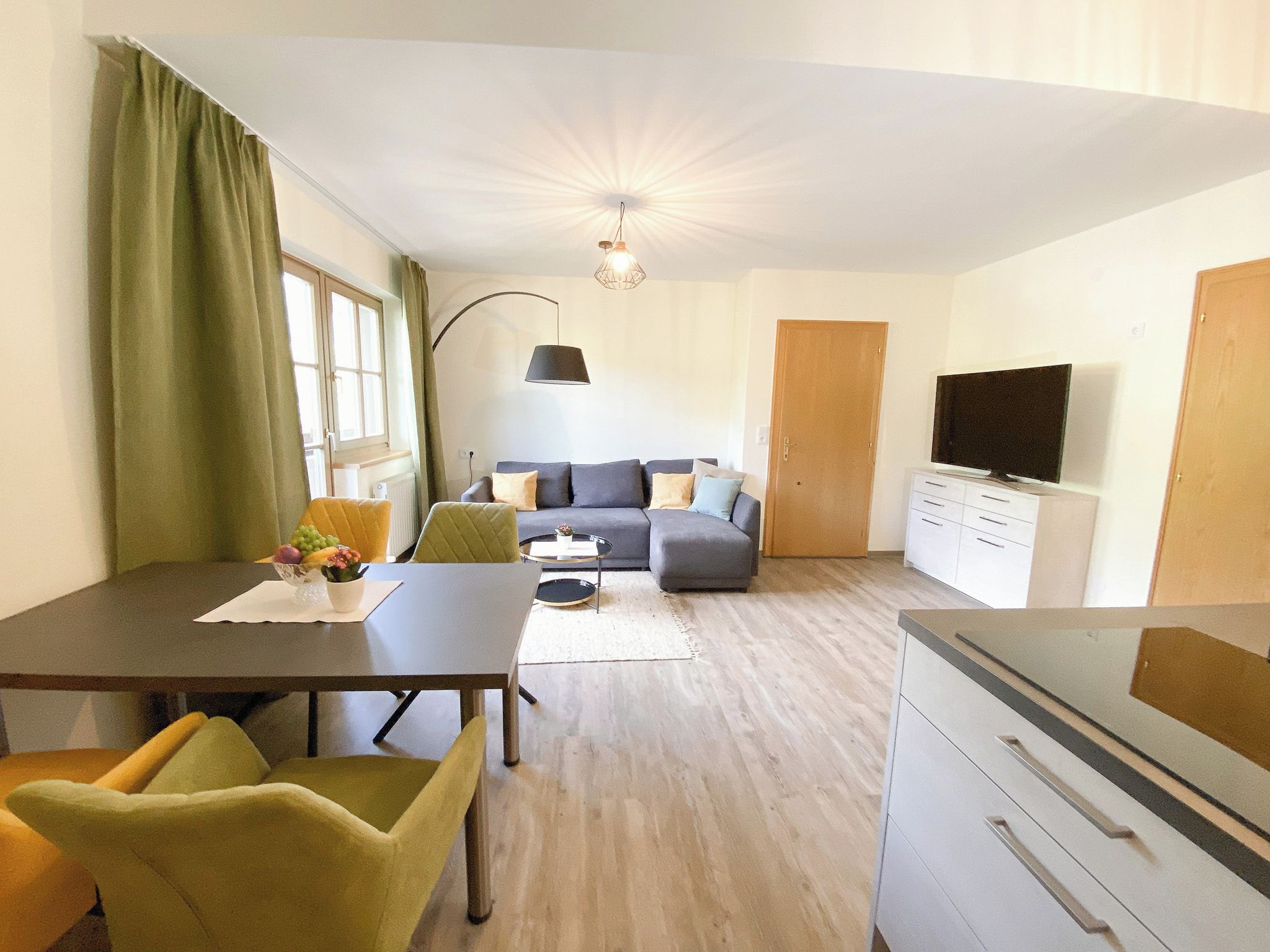 Una sala de estar moderna con un sofá, una mesa de comedor con sillas, un televisor y una zona de cocina.