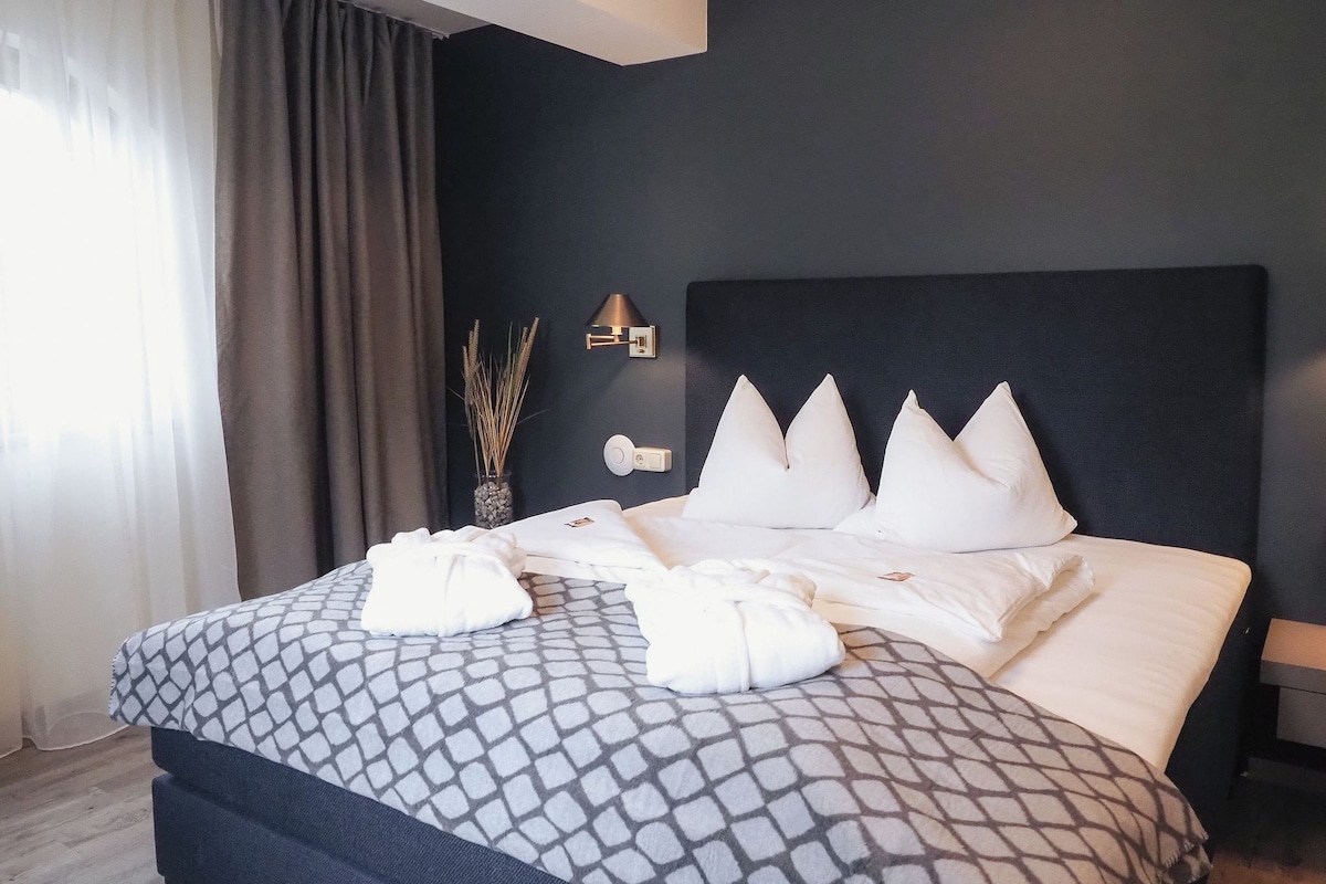 Ein modernes Hotelzimmer mit einem großen Bett, einem dunklen Kopfteil und einem Nachttisch mit einer Lampe.