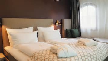 Una camera d'albergo con un letto grande, due cuscini, una testiera, una lampada da comodino, una finestra con tende e un comodino.