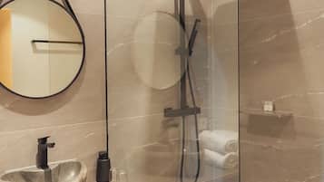 A modern bathroom with a stone sink, a round mirror, a handheld showerhead, and a towel rack.
